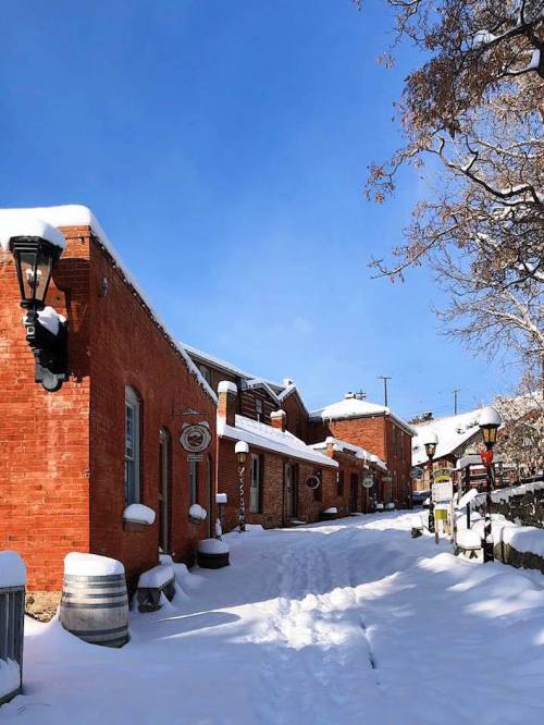 Snow-covered street lined with red brick buildings and vintage lamps under a clear blue sky.