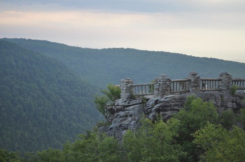 A stone railing overlooks a lush green mountain landscape under a cloudy sky.