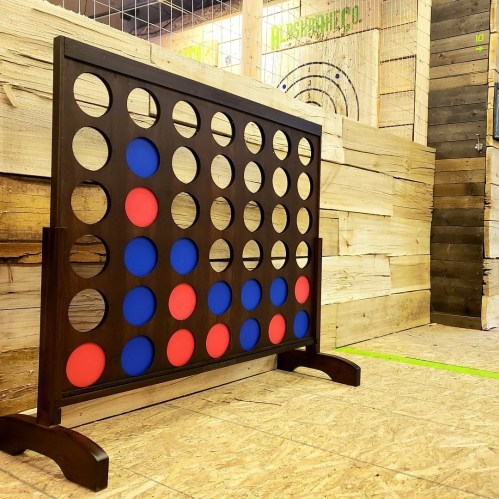 A large Connect Four game with red and blue discs set up in a wooden environment.