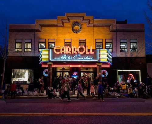 The illuminated Carroll Arts Center at dusk, bustling with people and festive decorations.