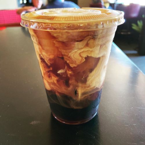 A clear cup filled with iced coffee, featuring swirls of cream creating a marbled effect.