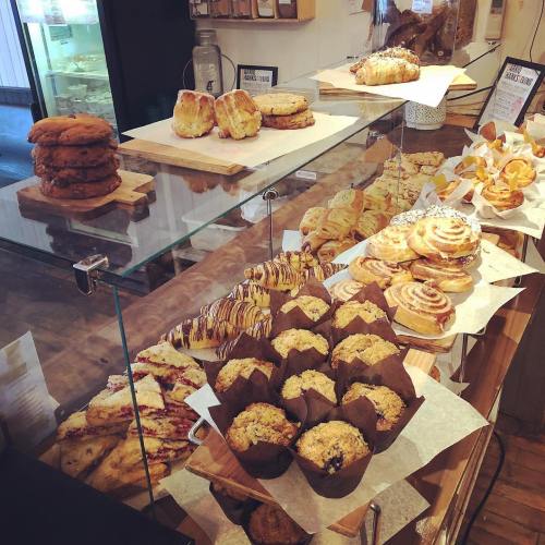 A display of various baked goods, including cookies, pastries, muffins, and cinnamon rolls, arranged on wooden trays.