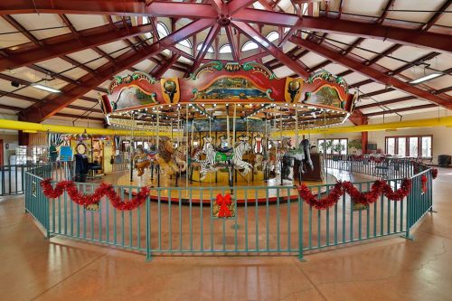 A colorful carousel with various animals, decorated with festive garlands, inside a spacious building.