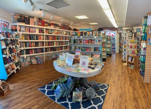 A cozy bookstore interior with shelves of books, a central display table, and wooden flooring.