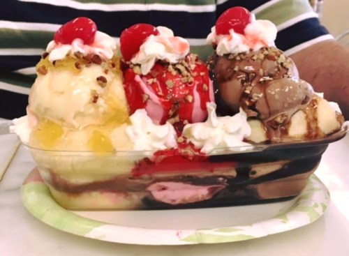 A colorful ice cream sundae with three scoops, whipped cream, cherries, nuts, and chocolate sauce in a dish.