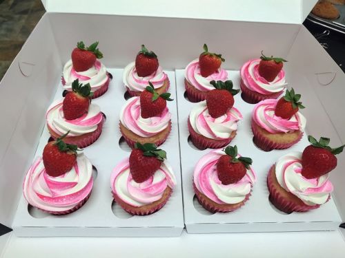 A box of cupcakes with pink and white swirled frosting, topped with fresh strawberries.