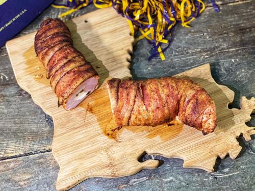 Bacon-wrapped meatloaf sliced on a wooden Louisiana-shaped cutting board, with festive decorations in the background.