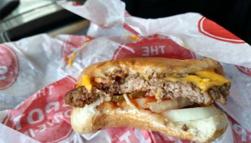 A half-eaten cheeseburger with melted cheese, lettuce, tomato, and onion, resting on red and white paper.