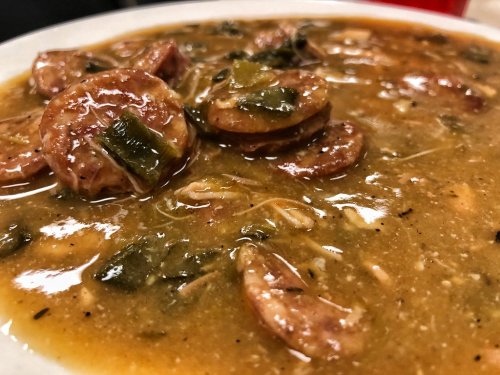 A close-up of a bowl of gumbo featuring sliced sausage, greens, and a rich, savory broth.