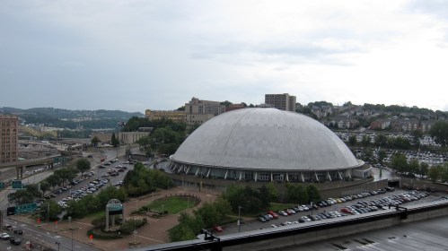 A large, dome-shaped building surrounded by greenery and parking lots, with a cloudy sky in the background.