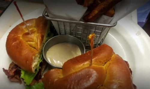 A close-up of two sandwiches with lettuce and a side of fries in a basket, accompanied by a small bowl of dipping sauce.