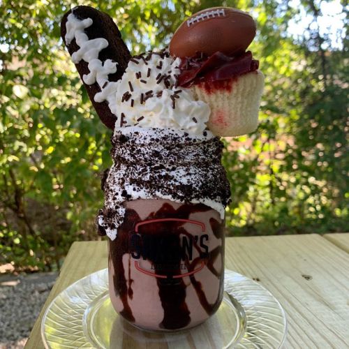 A decadent milkshake topped with whipped cream, chocolate sprinkles, a cupcake, and a mini football, served in a jar.