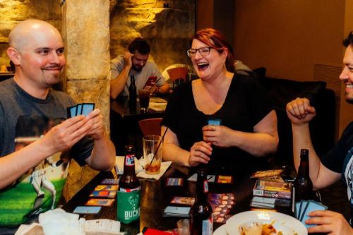 A group of friends enjoying a game night, laughing and playing cards at a table with drinks and snacks.