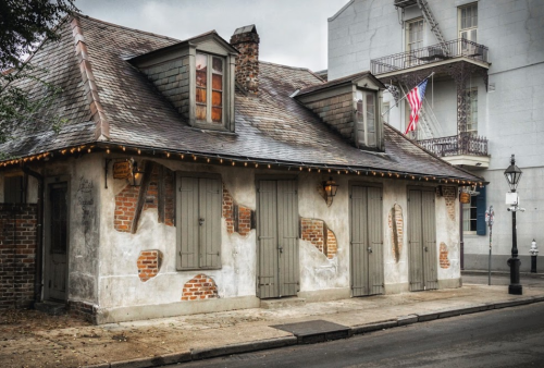 Historic building with weathered brick and wooden shutters, adorned with string lights and an American flag.