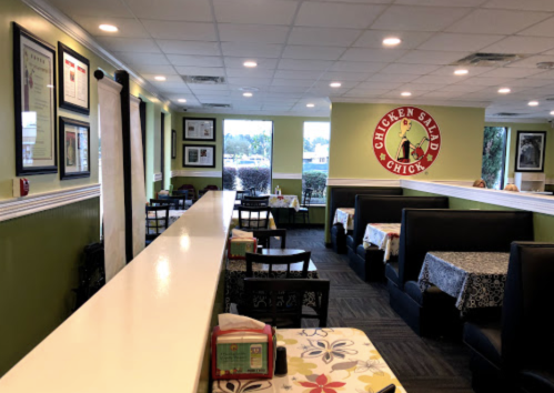 Interior of a casual restaurant with booths, tables, and a bright green wall featuring a Chicken Salad Chick logo.