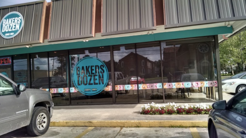 Exterior view of a bakery named "Bakers Dozen," featuring large windows and a colorful donut display.