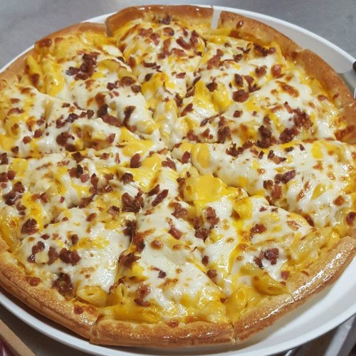 A pizza topped with melted cheese, bacon bits, and chunks of pineapple, sliced into equal pieces.