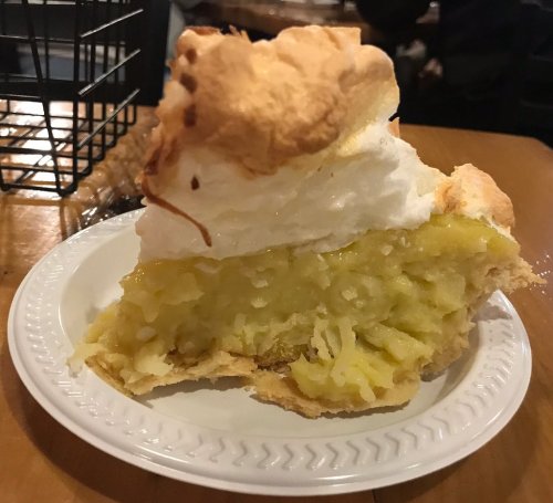 A slice of lemon meringue pie on a white plate, featuring a golden filling and a fluffy meringue topping.