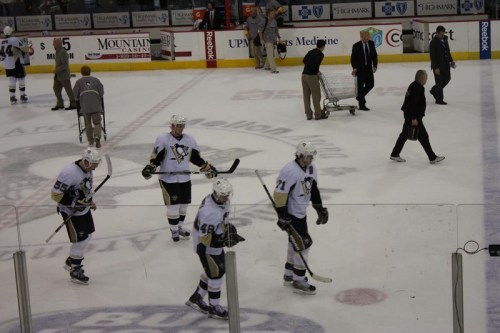 Pittsburgh Penguins players walk off the ice after a game, with staff and equipment visible in the background.
