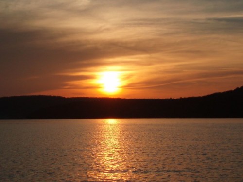 A serene sunset over a calm lake, with warm orange and yellow hues reflecting on the water's surface.