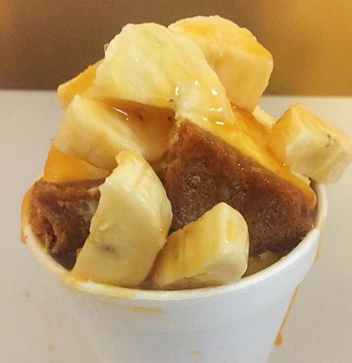 A cup filled with banana slices and chunks of bread drizzled with syrup.