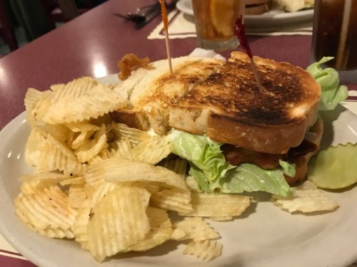 A toasted sandwich with lettuce and bacon, served with a side of potato chips on a plate.
