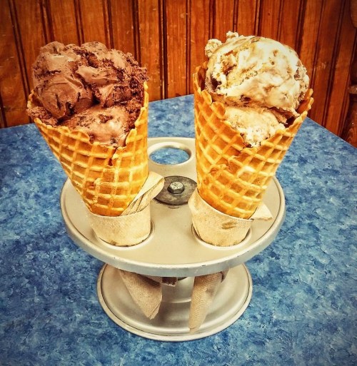 Two ice cream cones, one with chocolate and the other with vanilla, displayed in a metal holder on a blue table.