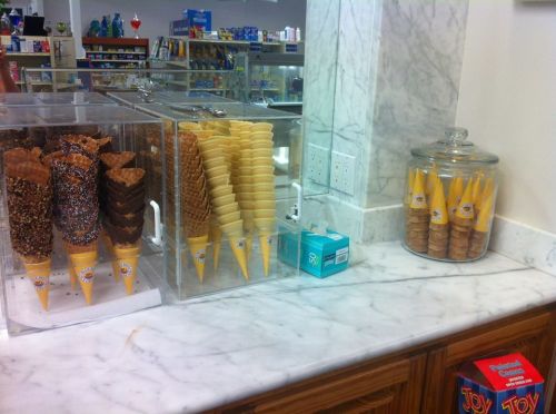 Display of various ice cream cones in a shop, including chocolate-dipped and plain cones, on a marble countertop.