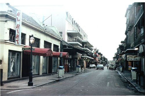 A quiet street scene featuring shops, balconies, and parked cars, with vintage signage in a historic district.