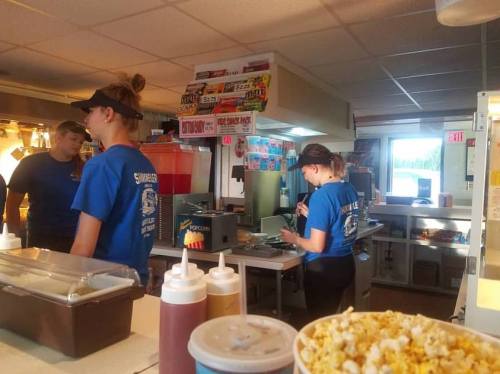 Staff members work behind a concession stand, preparing food and drinks, with popcorn in the foreground.