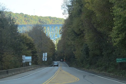A winding road surrounded by trees, leading towards a blue bridge in the distance.