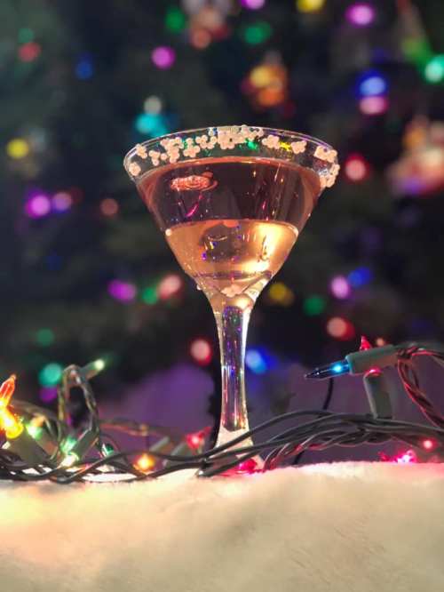 A festive cocktail in a glass with a sugared rim, surrounded by colorful holiday lights.