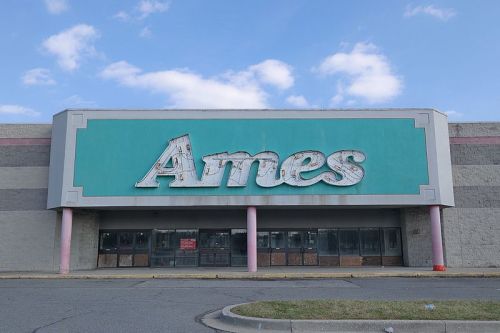Abandoned Ames store with a faded sign, featuring a turquoise facade and empty storefront under a blue sky.