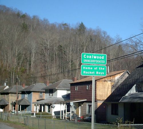 Sign for Coalwood, West Virginia, noting it as the home of the Rocket Boys, with houses and wooded hills in the background.