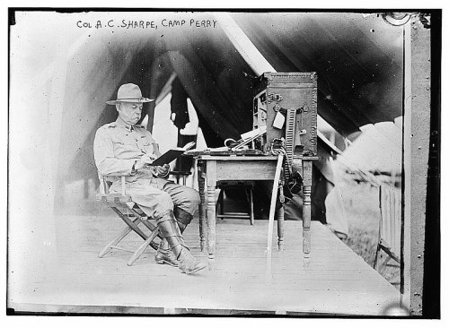 Colonel A.C. Sharpe sits at a table with a radio, reading at Camp Perry, early 20th century.
