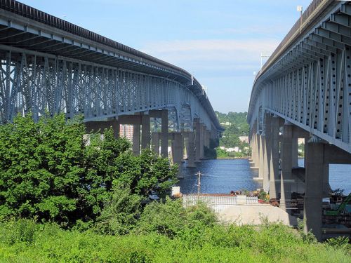 Two parallel bridges spanning a river, with greenery in the foreground and a clear blue sky above.