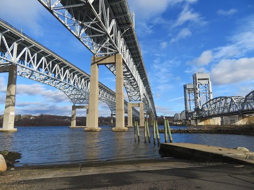 A view of a large steel bridge spanning over a river, with blue skies and clouds in the background.