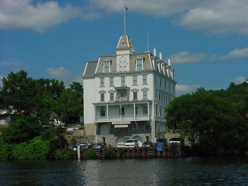 Historic white building with a peaked roof, surrounded by greenery and water, under a blue sky with clouds.