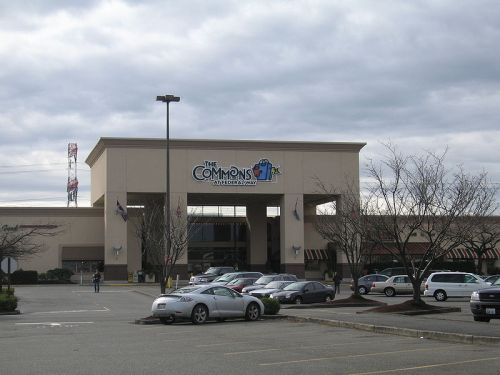 Entrance of The Commons shopping center with parked cars and cloudy sky in the background.