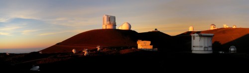 A panoramic view of observatories on a volcanic landscape at sunset, with domes and buildings silhouetted against the sky.