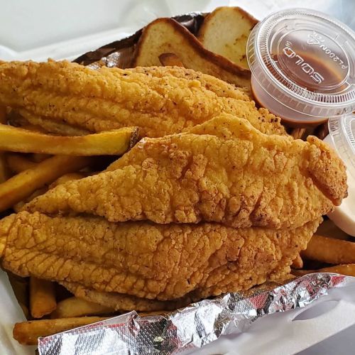 A takeout container with two fried fish fillets, French fries, and two dipping sauces.
