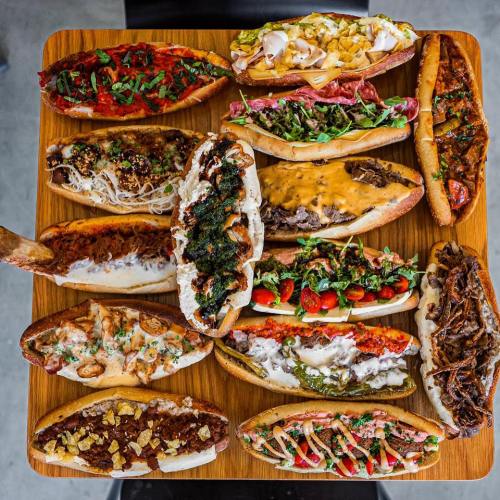 A wooden platter filled with a variety of colorful hot dogs topped with different ingredients and garnishes.