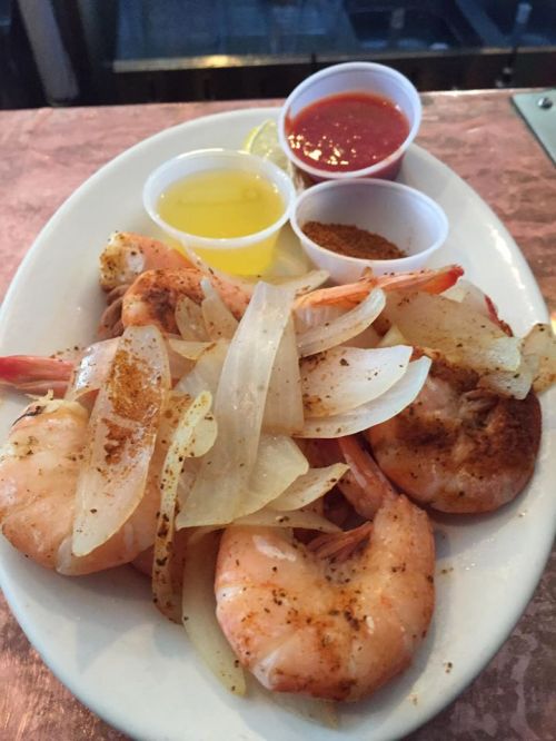 A plate of seasoned shrimp with onions, accompanied by lemon, cocktail sauce, and a spice blend.