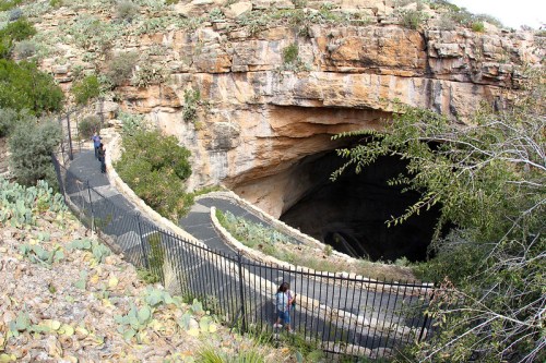 A winding path leads to a large cave entrance, surrounded by rocky terrain and vegetation.