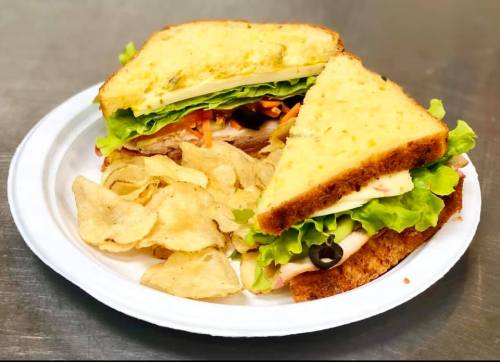 A plate with a sandwich filled with lettuce, turkey, and olives, served with a side of potato chips.