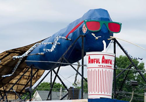 A large blue creature with sunglasses and a giant drink cup, featuring the text "Awful Awful - It's a Drink."