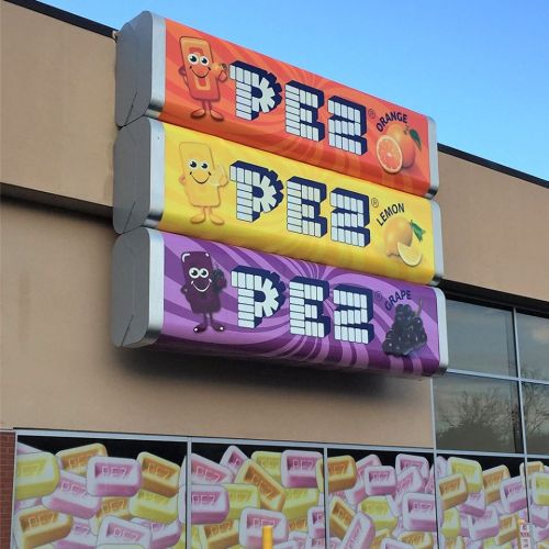 Colorful PEZ candy sign featuring orange, lemon, and grape flavors with cartoon characters on a storefront.