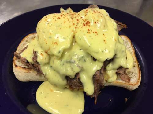 A slice of bread topped with tender beef and a creamy yellow sauce, garnished with a sprinkle of paprika.