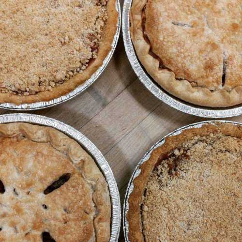 Three freshly baked pies in aluminum pans, featuring crumbly tops and golden crusts, arranged in a circular pattern.