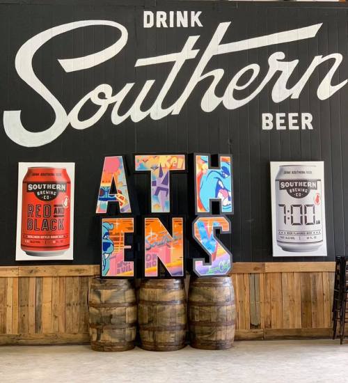 A wall featuring "Drink Southern Beer" with colorful letters spelling "ATHENS" and beer posters on either side.